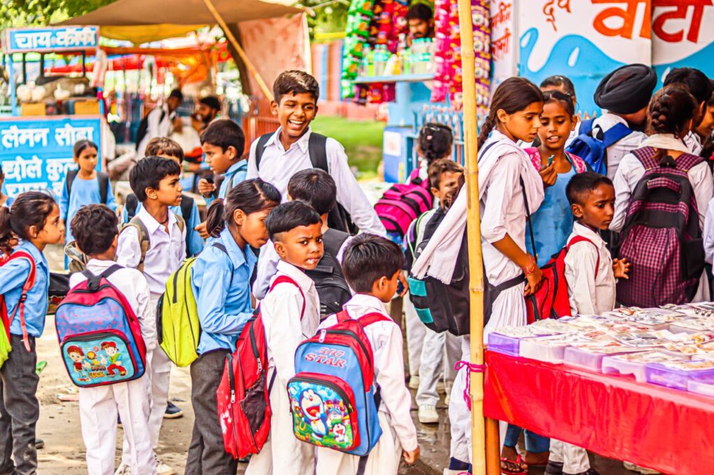 Legal Awareness Camp Organized on Public Rights in Old Town Bhubaneswar Group of children in uniforms with backpacks queuing at a market stall outdoors.